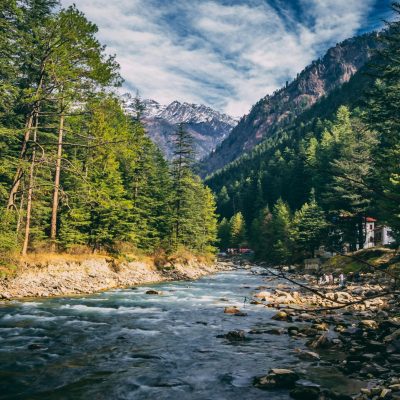 Beautiful landscape of river flowing through coniferous forest in Kasol, India with mountains in the background.